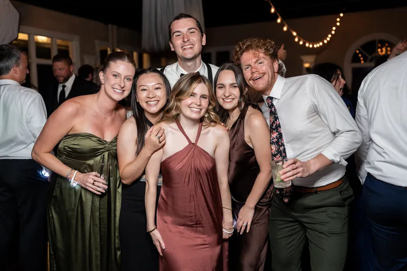 A group of five guests smile together at The White Room, dressed in formal wear ranging from olive to burgundy tones.
