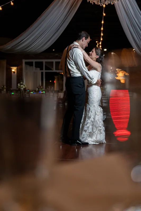 Two people embrace under flowing white drapes strung with golden lights at The White Room, framed by the venue's elegant interior.