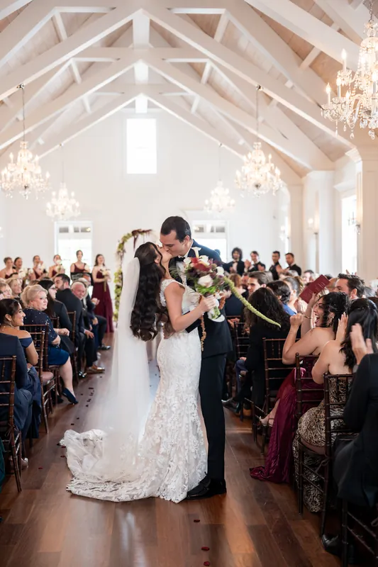 Andrew and Emme grin widely while surrounded by beaming bridesmaids and groomsmen holding bouquets on a tree-lined courtyard.