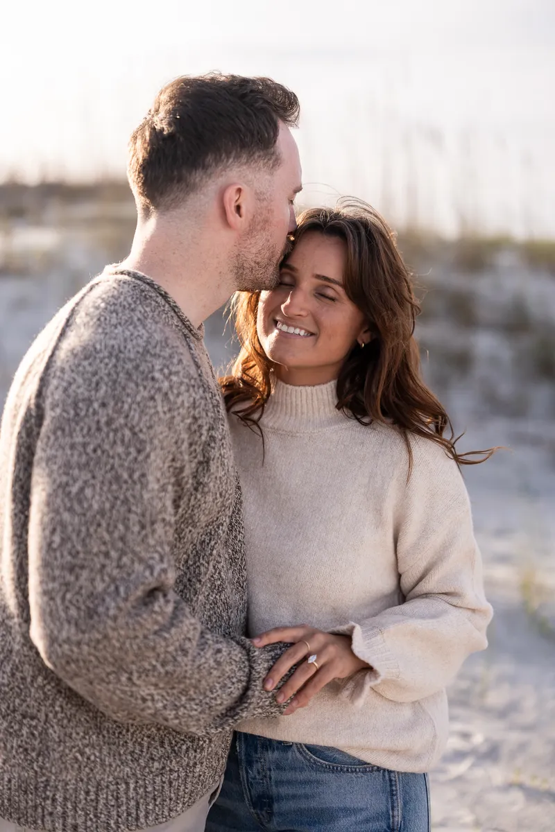 Eric and Anastasia share an intimate moment during golden hour, with Eric gently kissing her forehead as she smiles warmly.