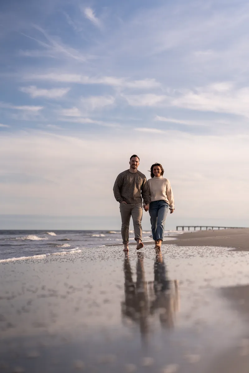 Couple walking hand in hand along Anastasia Beach with reflections in wet sand