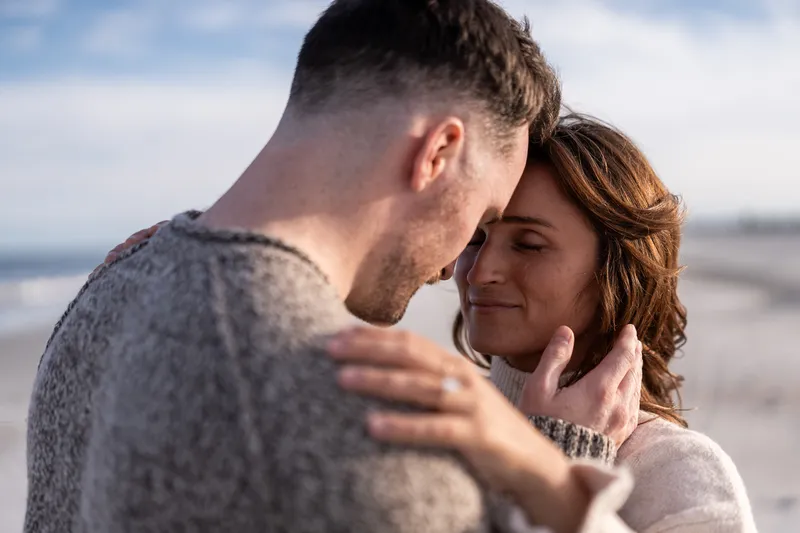 Eric and Anastasia share an intimate forehead-to-forehead moment during their beach engagement session, with soft golden light illuminating their tender embrace.