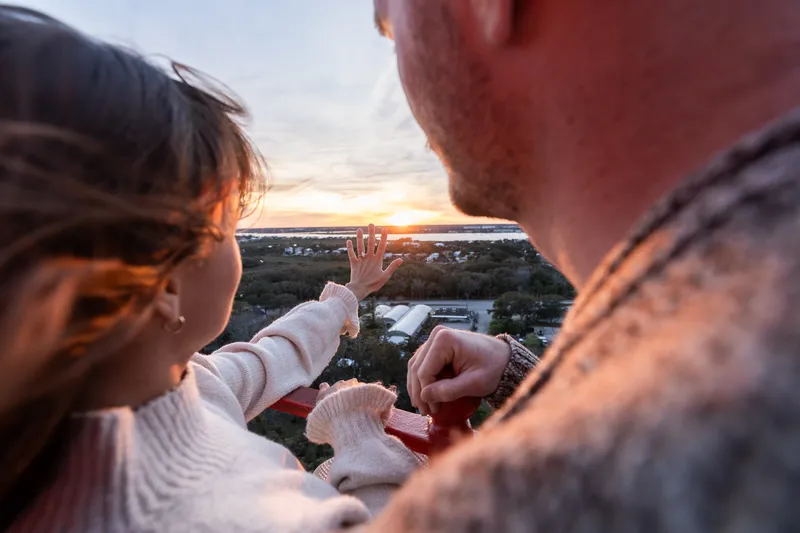 An intimate moment captured from above as Eric proposes to Anastasia at sunset, with her hand reaching toward the golden light on the horizon.
