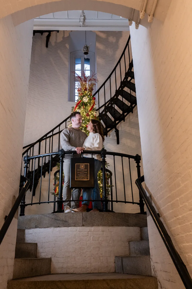 Eric and Anastasia share an intimate moment on a historic stone staircase decorated with Christmas garland and lights.