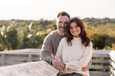 Eric and Anastasia share an intimate moment on a sandy beach during golden hour, gazing lovingly at each other while walking barefoot.