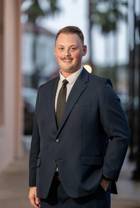 Eric stands in a navy blazer and tie on a Downtown St Augustine street lined with colonial architecture and palm trees.