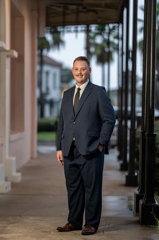 Eric walks down a covered portico with arched doorways and palm trees visible beyond in Downtown St Augustine.