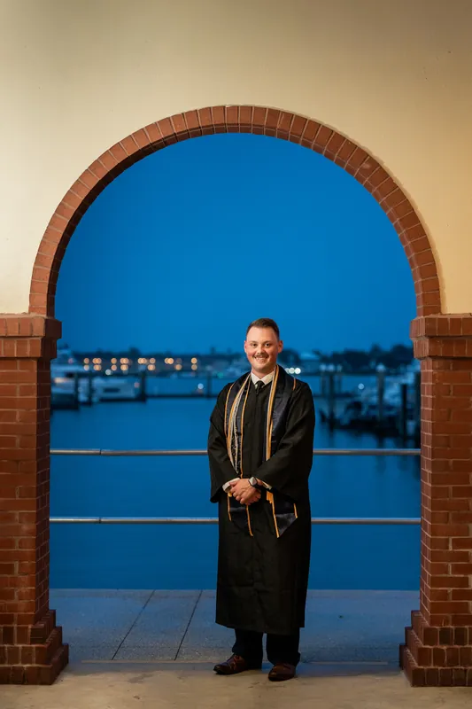 Someone in a black robe stands beneath a brick archway framing blue water at dusk in Downtown St Augustine.