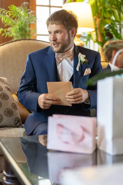 Groom in blue suit holding card sitting in elegant lounge with plants
