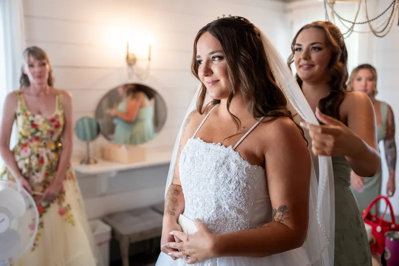 A person in a white lace halter gown stands with others in an indoor venue, smiling while adjusting their dress.
