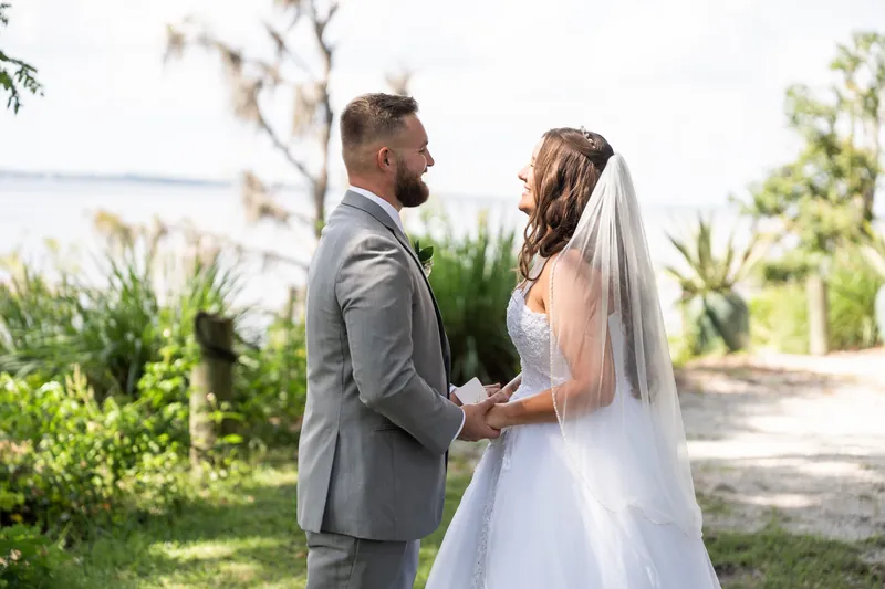 The couple exchanges vows outdoors at La Venture Grove, surrounded by lush greenery, with one partner in gray and the other in white.