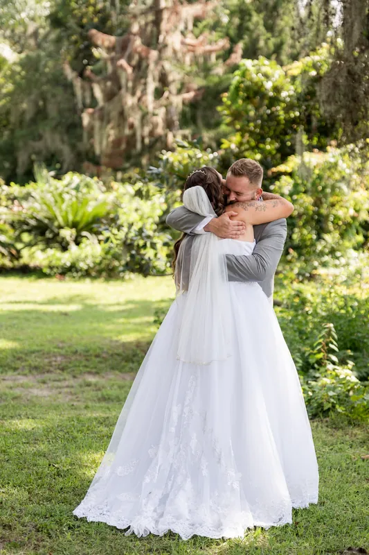 Two people embrace under Spanish moss-draped trees at La Venture Grove, the person in white resting their head on their partner's shoulder.