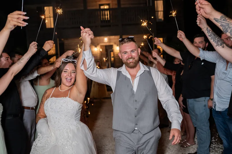 The newlyweds lead guests down a lit pathway while friends and family wave sparklers overhead in celebration.