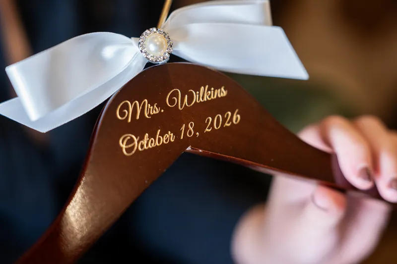 A wooden hangar labeled "Mrs. Wilkins" holds a white silk bow and a diamond ring on October 18, 2026.