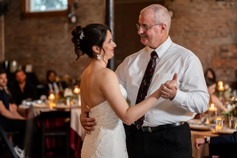 Woman in a sleeveless white gown dancing with an older man in a light shirt and tie during the reception at Brick and Beam, Jacksonville.