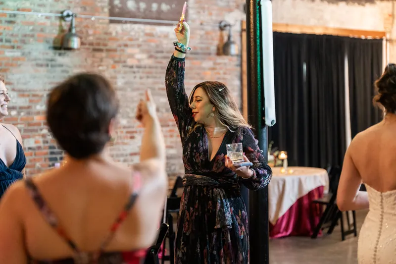 A woman in a dark patterned dress raises her arm in celebration during the reception at Brick and Beam's brick-walled venue.