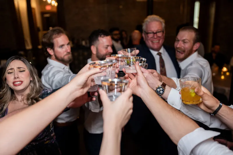 Multiple hands clink glasses together in a toast at the industrial brick venue.