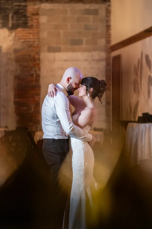 Faith and Christian kiss intimately against exposed brick at Brick and Beam, with warm accent lighting framing the moment.