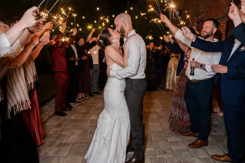 Guests holding sparklers create a glowing tunnel as Faith and Christian dance together beneath strung lights at Brick and Beam's final celebration.
