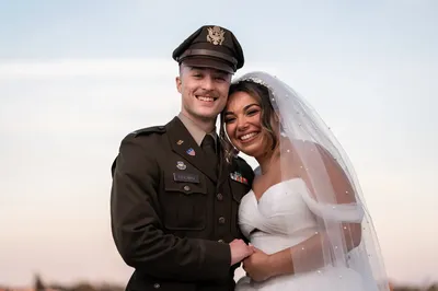 Gabi and Dawson smiling together at sunset, Dawson in his Army dress uniform and Gabi in her white wedding gown with pearl-studded veil
