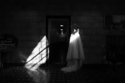 Bride in flowing white gown stands in dramatic black and white venue lighting