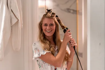 Woman styling hair with curling iron in bright bathroom mirror