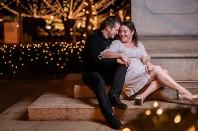 Couple cuddling on steps with Nights of Lights behind them