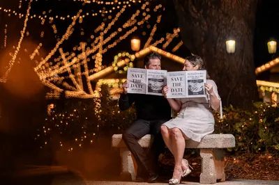 Giselle and Duncan reading save-the-date newspapers on bench
