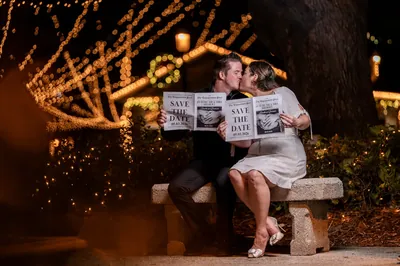 Giselle and Duncan kissing on bench with save-the-date newspapers