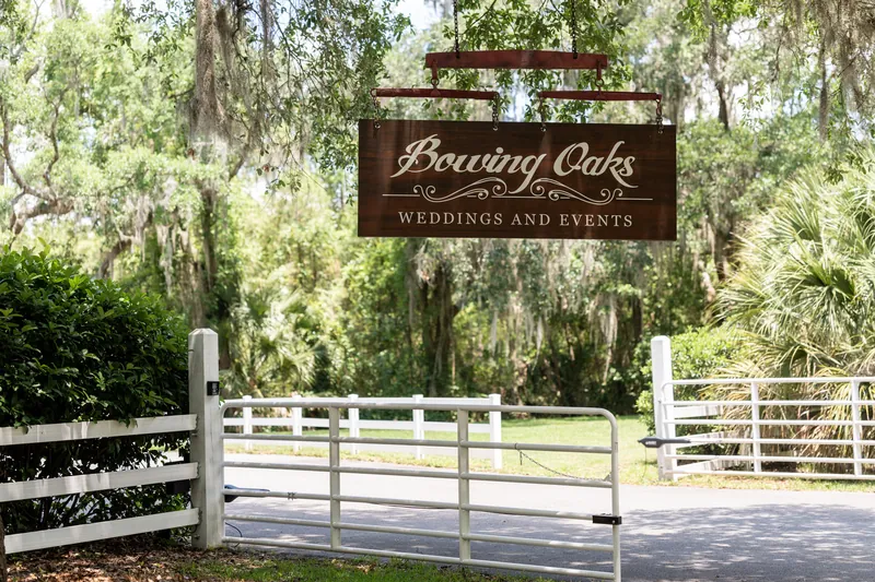 Boaring Oaks wedding venue sign mounted on wooden fence gate with white railings and lush trees.