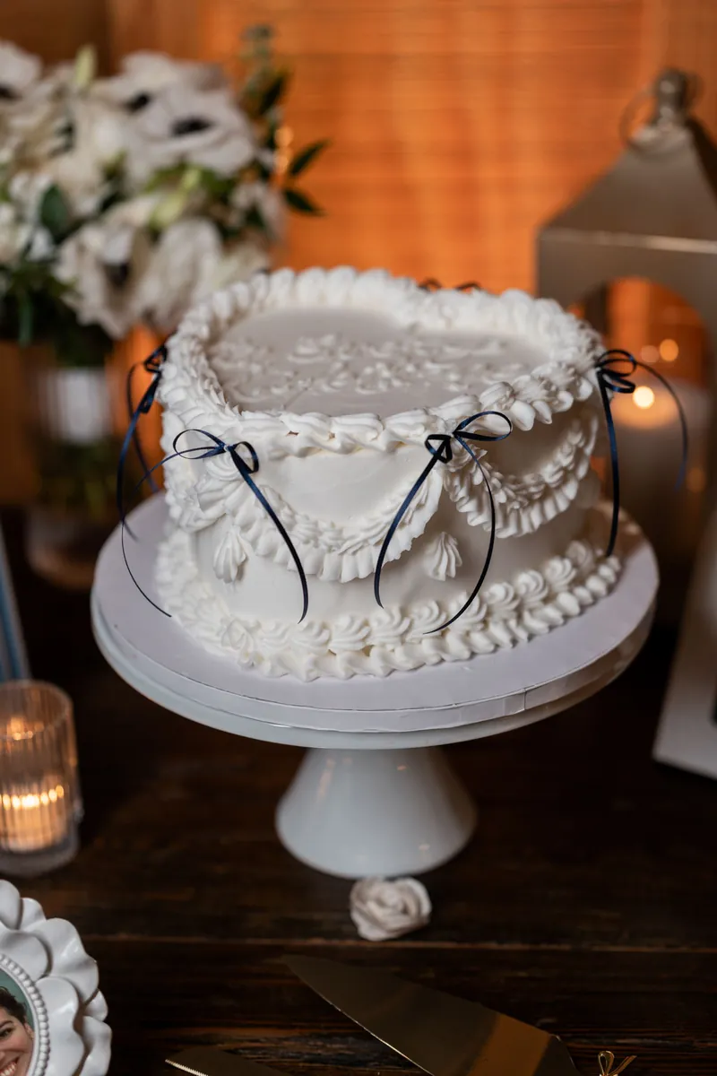 Two-tier white wedding cake with pearl beading and black ribbon detail on a pedestal display table.