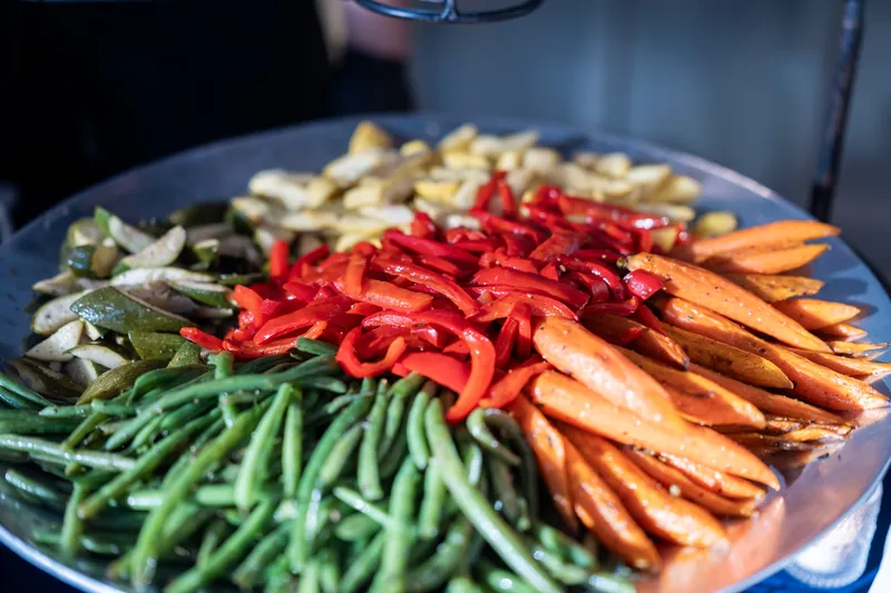 Blue platter with arranged vegetables including green beans, red peppers, and orange carrots with dip.