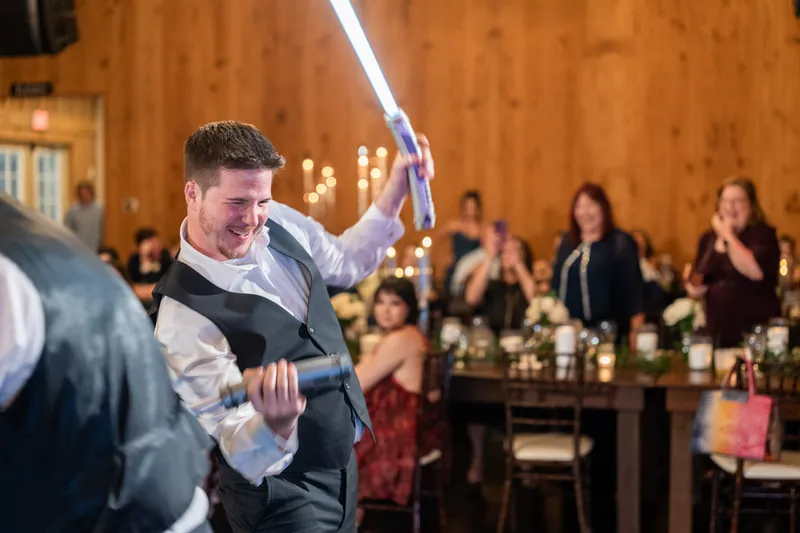 Duncan swings a light saber while dancing at the reception, with guests seated at tables in the background.