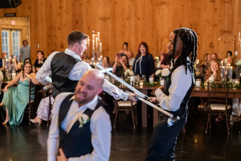 Duncan and a guest duel with glowing light sabers on the dance floor as wedding attendees watch.