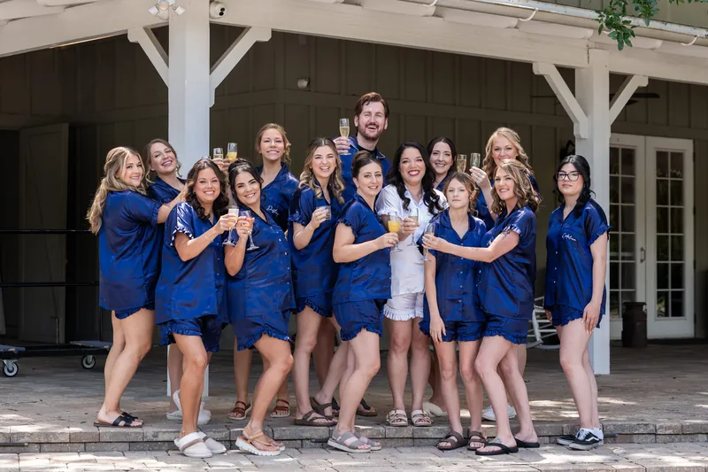 Giselle's bridesmaids in matching blue dresses stand together on a wooden pavilion, smiling at the camera.