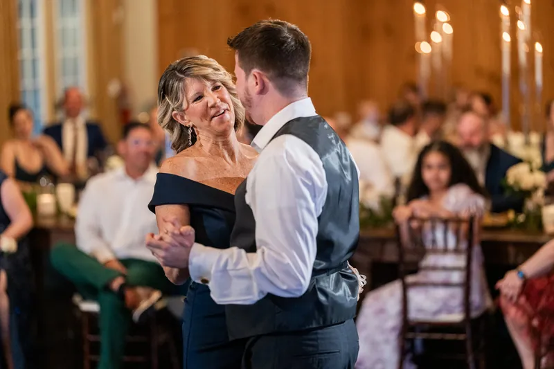 Duncan dances with a woman in an off-shoulder navy dress while guests watch from their tables.