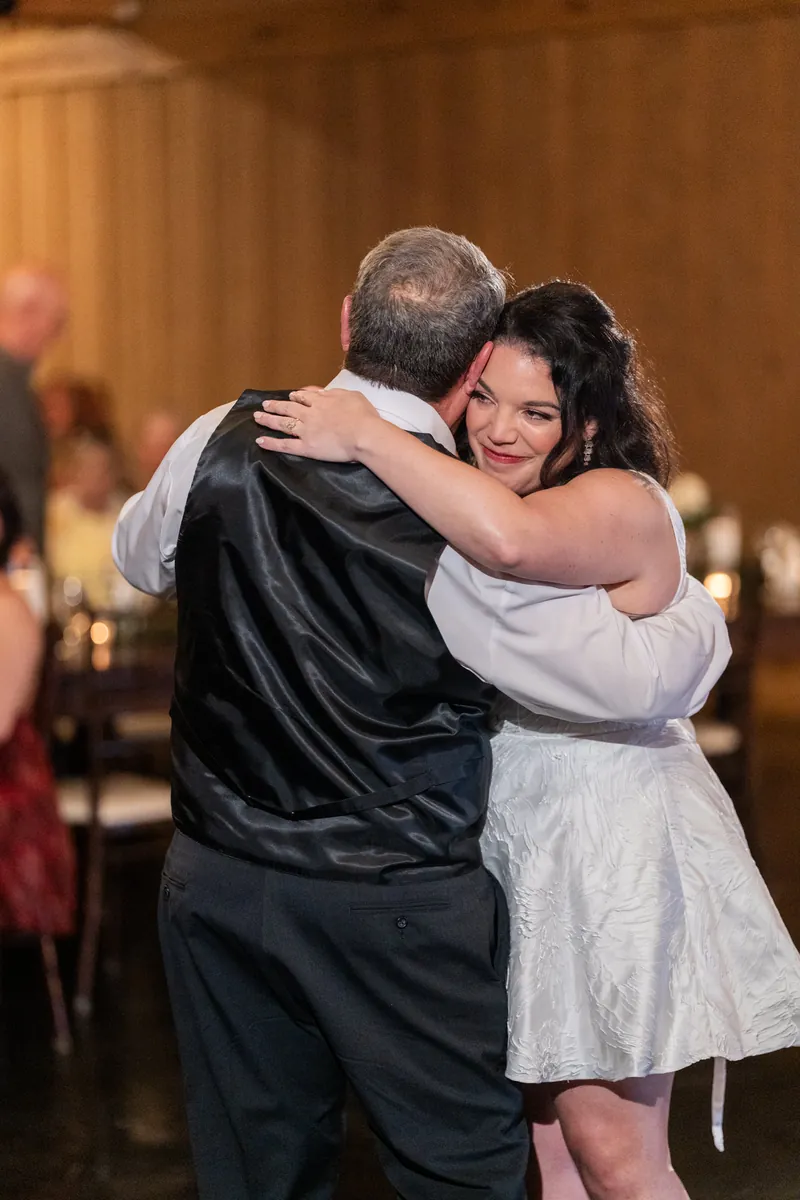 Giselle hugs a male guest in a white dress at her wedding reception.