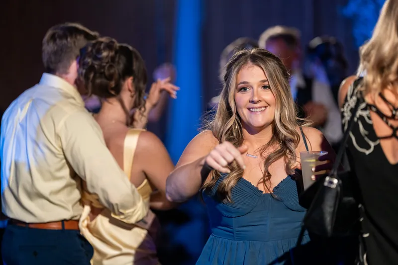 Wedding guests dance together at the reception under blue lighting.
