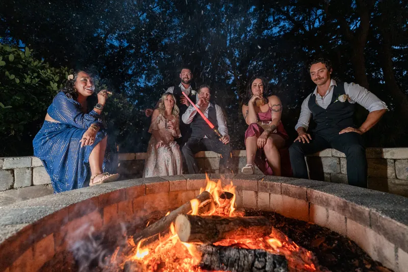 Wedding guests gather around a blazing fire pit under a starlit sky.