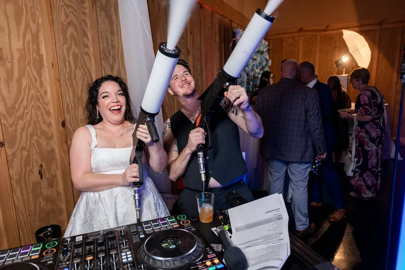 Giselle in white stands at the DJ booth while guests celebrate behind her.