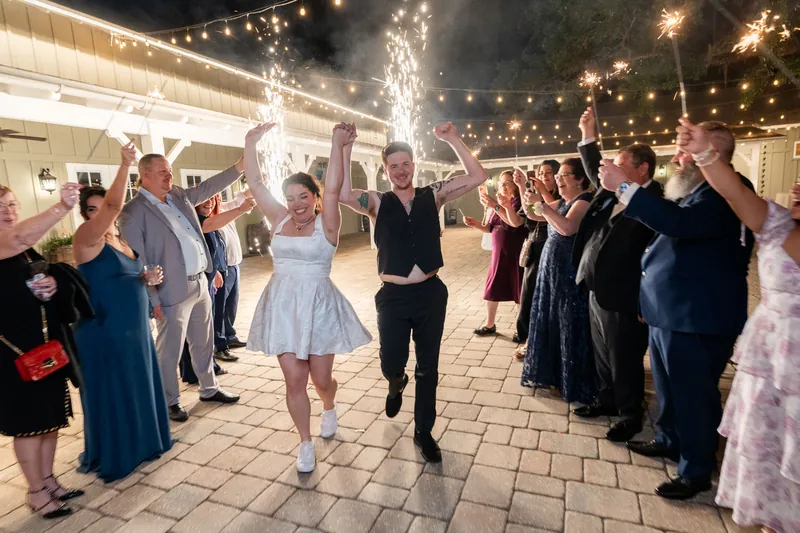 Giselle & Duncan run through sparkler tunnel lined with cheering guests outdoors.