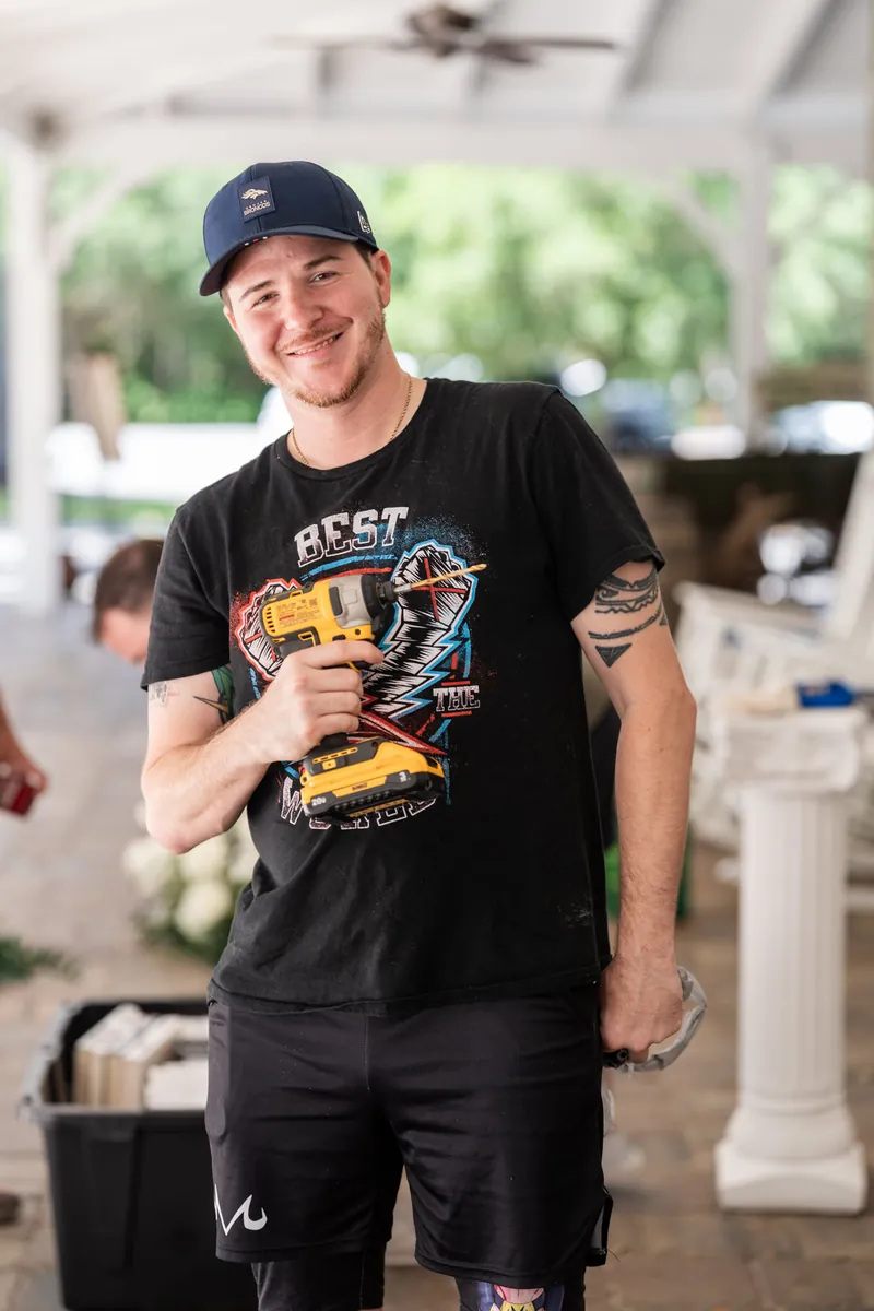 Duncan grins while holding a microphone in a black graphic tee and navy cap at the reception.