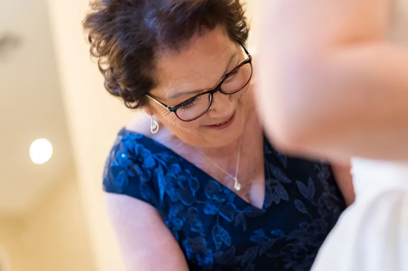 Woman wearing glasses and blue velvet wrap smiles warmly during wedding reception.