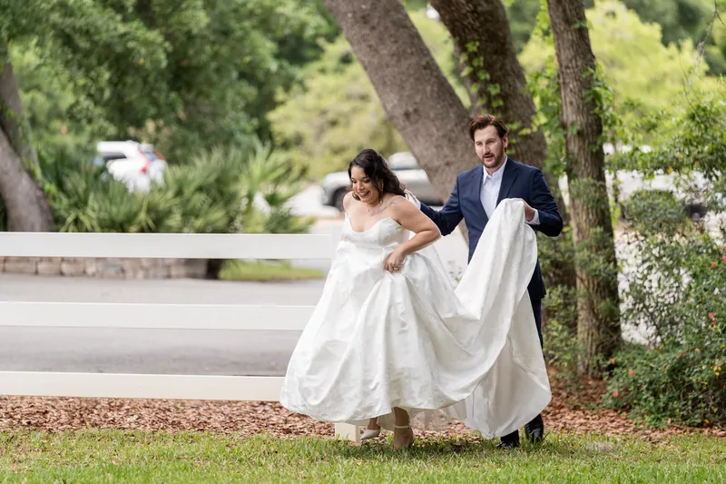 Giselle and Duncan walk together under a large tree, her white gown flowing behind them on the lawn.