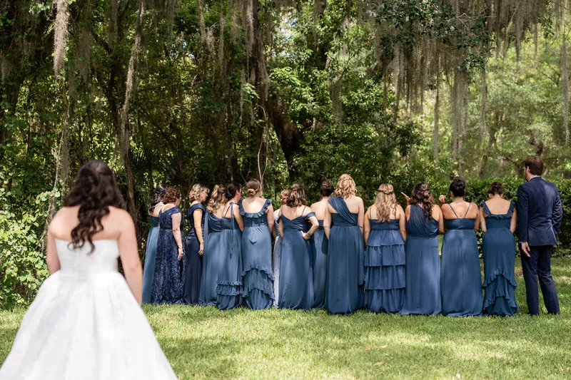 Giselle in white dress stands before line of bridesmaids in blue dresses and groomsman in dark suit.