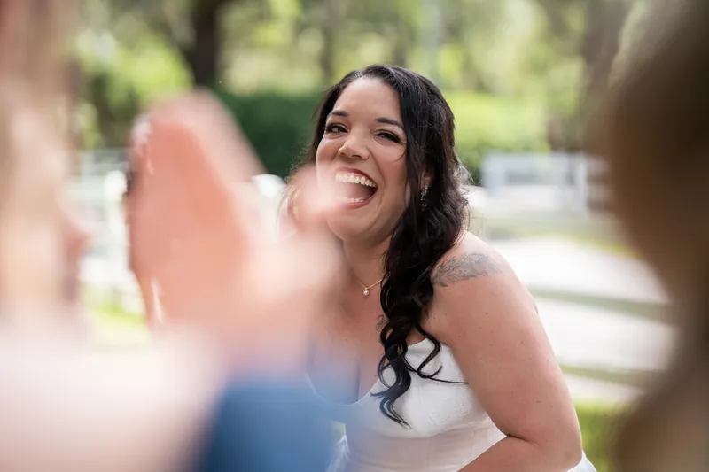 Giselle smiles during conversation with bridesmaids at garden wedding surrounded by greenery.