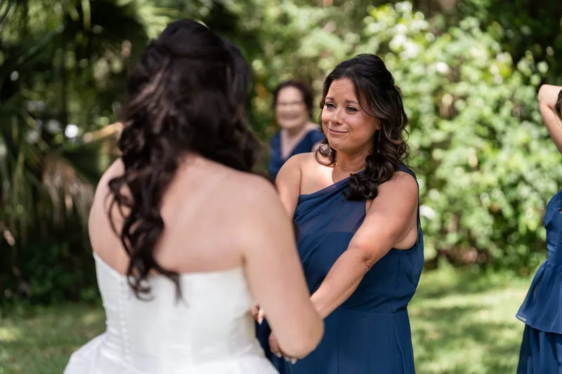 Giselle in white strapless gown smiles while holding hands with bridesmaid in navy dress outdoors.