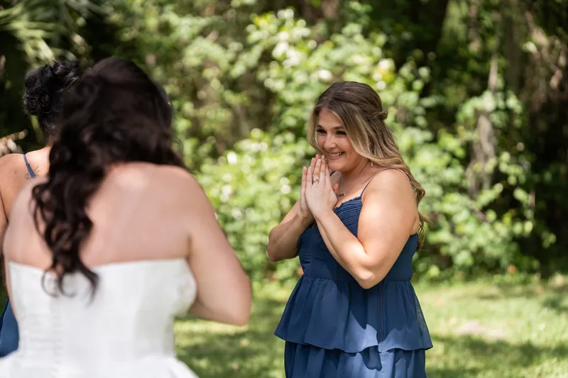 Bridesmaid in navy dress reacts with surprise and emotion while Giselle watches in white gown.