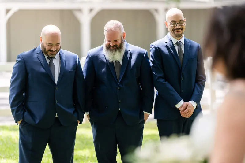 Duncan and two groomsmen in navy suits walk toward Giselle holding her bouquet.