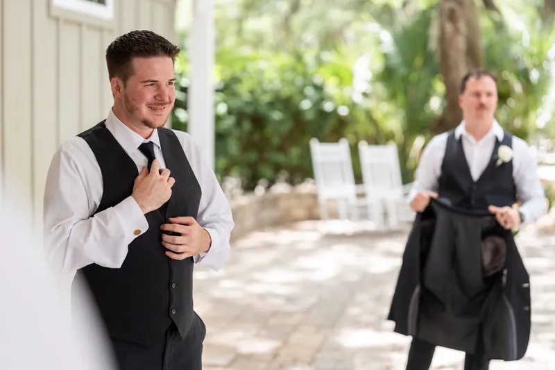 Duncan adjusts his tie while speaking outdoors at a covered porch venue.